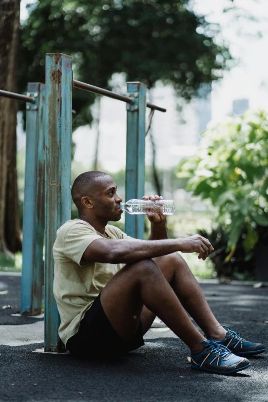 a man sitting on the ground drinking water, a portrait, by Fletcher Martin, pexels contest winner, wearing fitness gear, sitting on bench, man is with black skin, in sao paulo