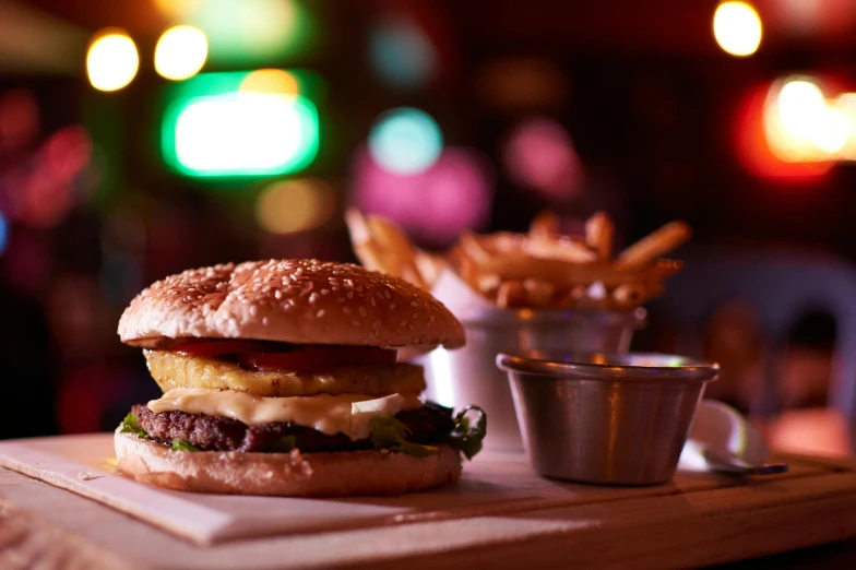 a hamburger sitting on top of a cutting board next to french fries, dimly lit dive bar, dazzling lights, stacks, 🦩🪐🐞👩🏻🦳