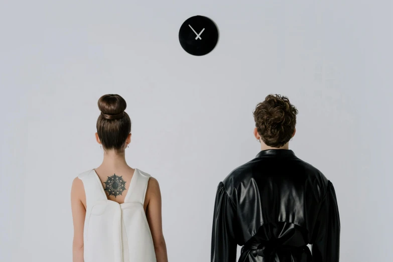 a man and a woman standing in front of a clock, a tattoo, inspired by Marina Abramović, trending on pexels, minimalism, all black matte product, people watching around, elegantly dressed, enamel