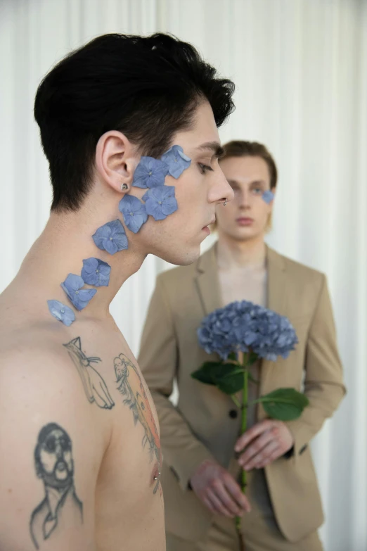 a couple of men standing next to each other, an album cover, by Jessie Alexandra Dick, aestheticism, huge earrings and queer make up, blue - petals, tattoo, ignant