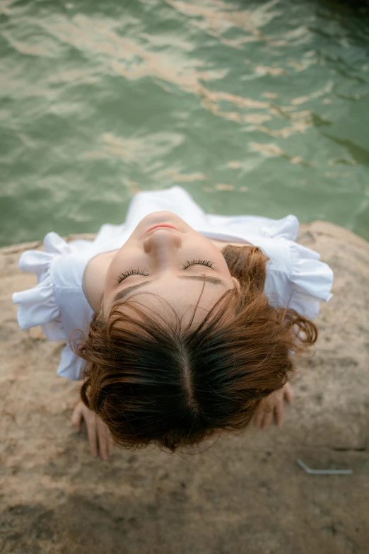 a woman laying on top of a rock next to a body of water, inspired by Yu Zhiding, unsplash, renaissance, asian face, high angle closeup portrait, [ floating ]!!, shy looking down