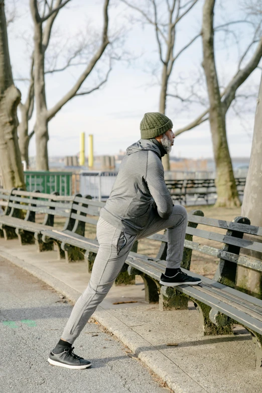 a man sitting on a bench in a park, inspired by Michael Gustavius Payne, happening, dynamic stretching, he also wears a grey beanie, in new york city, green legs