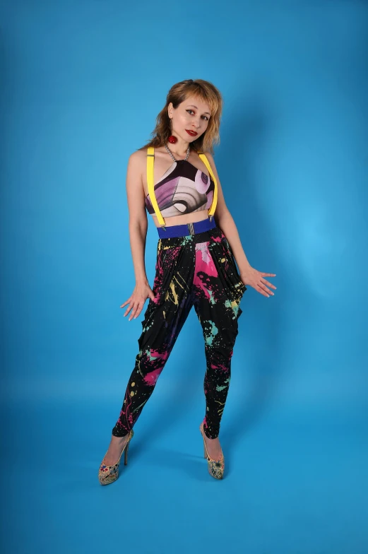 a woman standing in front of a blue background, inspired by Tadanori Yokoo, pop art, purple bridges with leggins, wearing overalls, official store photo, kylie minogue as barbarella