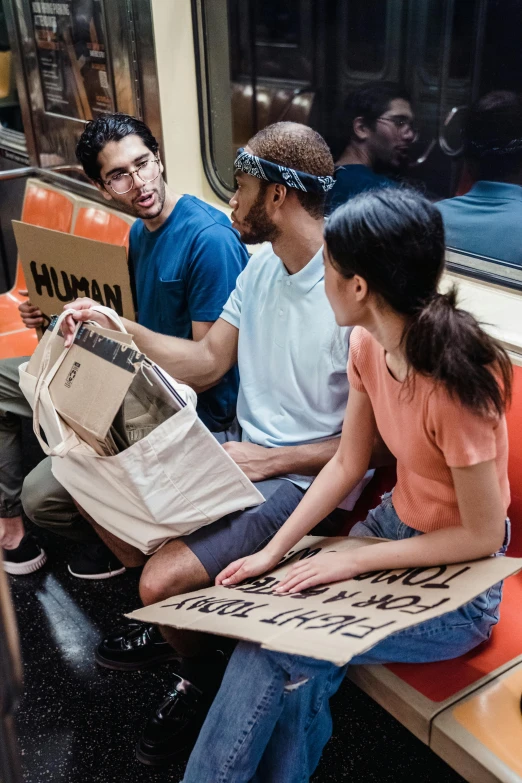 a group of people sitting next to each other on a train, graffiti, sustainable materials, bags, placards, instagram picture