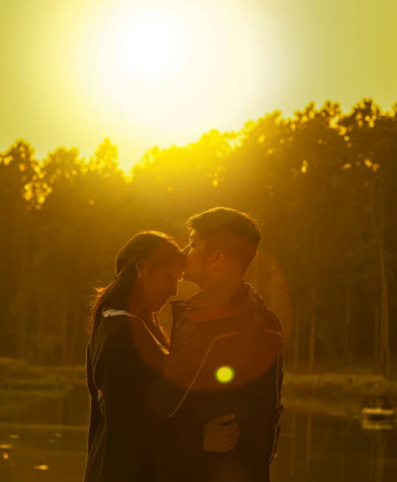 a couple standing next to each other in front of a lake, pexels contest winner, romanticism, golden sunlight, movie frame still, yellow sky, in front of a forest background