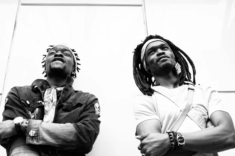 a couple of men standing next to each other, a black and white photo, unsplash, black arts movement, dreadlocks, album art for char zulu, facing sideways, brightly lit