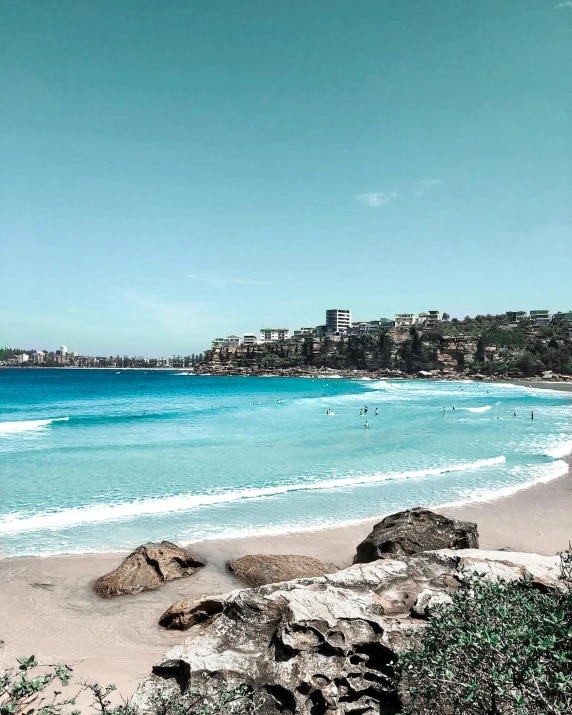 a man riding a surfboard on top of a sandy beach, bondi beach in the background, purple and blue colour palette, a photo of the ocean, cliffs