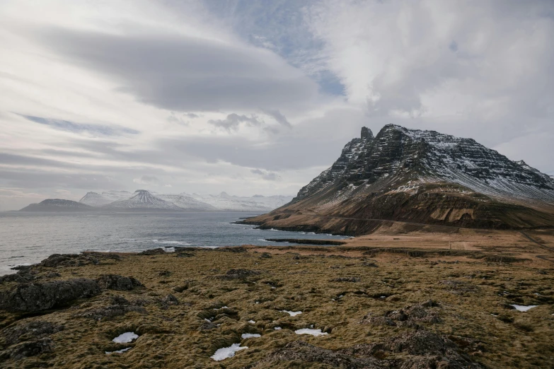 a mountain covered in snow next to a body of water, by Hallsteinn Sigurðsson, pexels contest winner, hurufiyya, views to the ocean, devils horns, conde nast traveler photo, brown