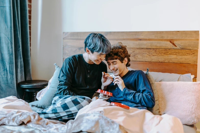 a couple of people sitting on top of a bed, a cartoon, trending on pexels, gay, south korean male, wearing pajamas, male teenager