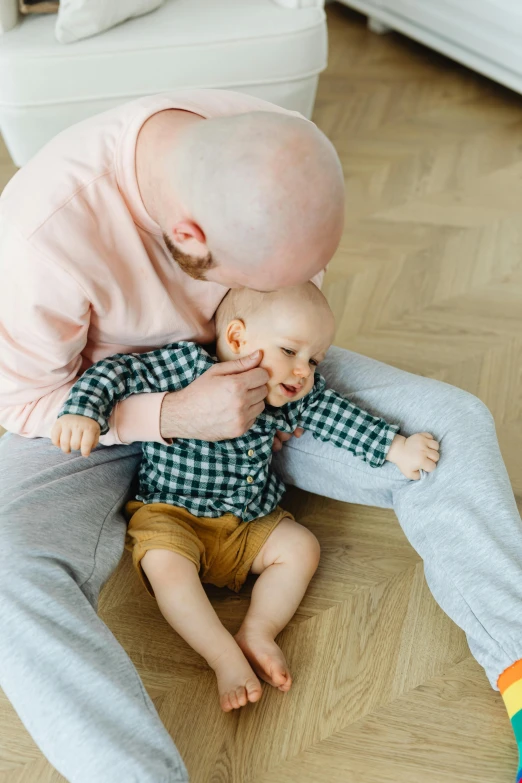 a man sitting on the floor holding a baby, by Jan Tengnagel, pexels contest winner, dada, small blond goatee, hugging each other, a bald, 15081959 21121991 01012000 4k