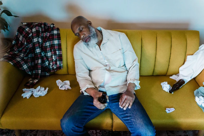 a man sitting on top of a yellow couch, by Paul Davis, pexels contest winner, portrait of an alcoholic, atiba jefferson, two exhausted, earl nore