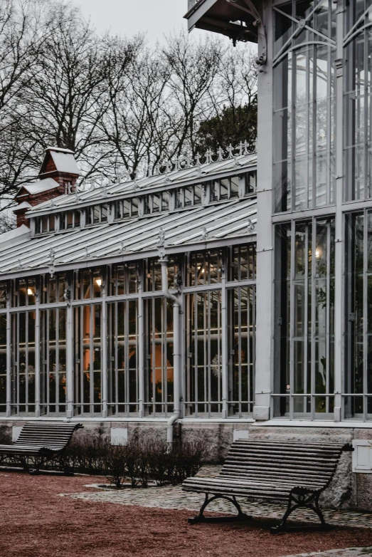 a couple of benches sitting in front of a building, an album cover, inspired by Constantin Hansen, pexels contest winner, glass greenhouse, winter setting, stockholm, exterior botanical garden