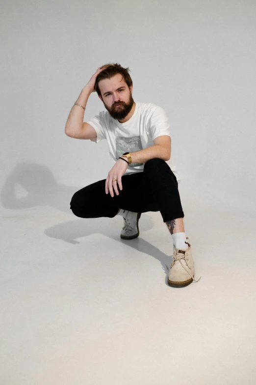 a man sitting on top of a white floor, an album cover, dressed in a white t-shirt, light beard, sydney hanson, with hands in pockets