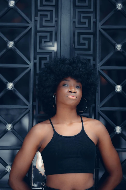 a woman standing in front of a metal door, by Lily Delissa Joseph, pexels contest winner, afrofuturism, short black curly hair, all black matte product, handsome girl, sitting down casually
