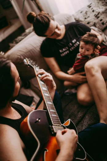 a group of people sitting on a couch playing guitar, by Daniel Seghers, pexels, husband wife and son, asher duran, babies in her lap, lesbians