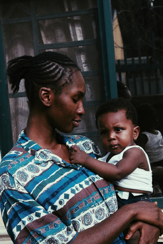 a woman holding a child in her arms, an album cover, by Ingrida Kadaka, pexels contest winner, afropunk, grainy footage, woman with braided brown hair, slide show