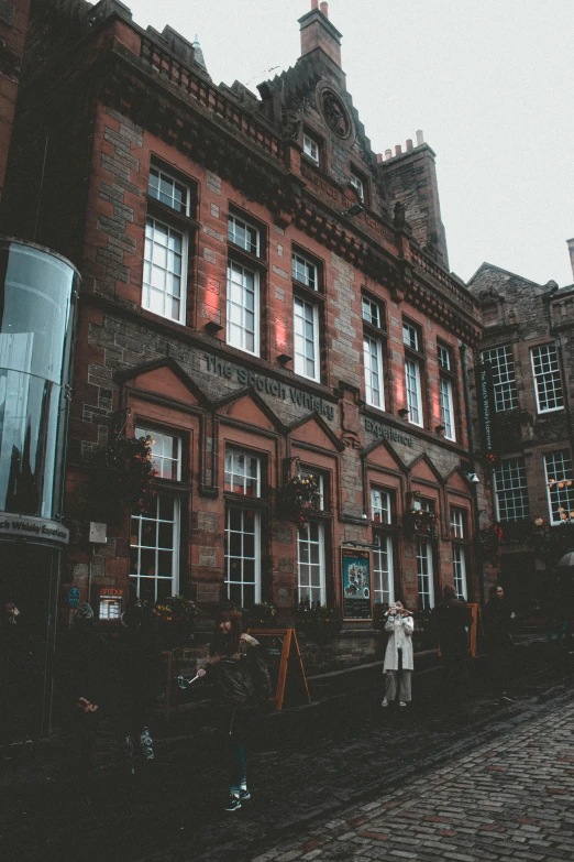 a couple of people that are standing in front of a building, by IAN SPRIGGS, pexels contest winner, scottish style, slight overcast lighting, detailed buildings, a cozy