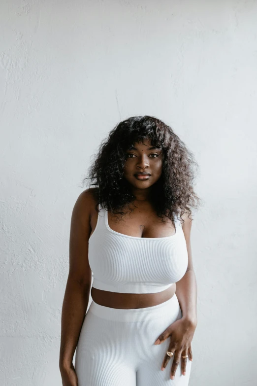 a woman standing in front of a white wall, trending on pexels, renaissance, sports bra, lizzo, natural hair, thicc build
