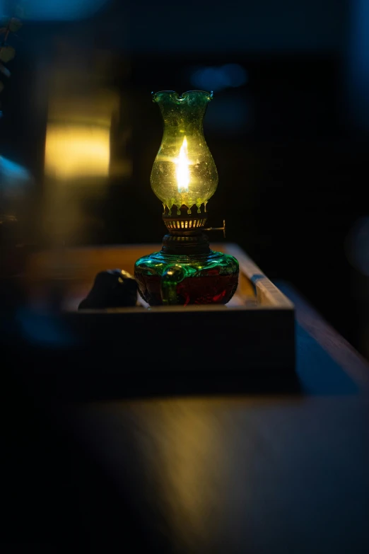 a lit candle sitting on top of a wooden table, green light, edison bulb, nightcap, indoor picture