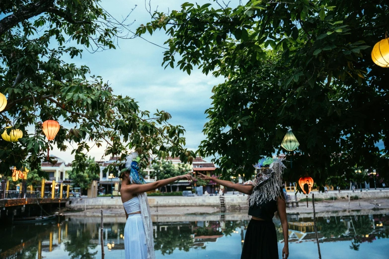a couple of women standing next to each other near a body of water, unsplash, happening, in style of lam manh, puppet on a string, wearing a paper crown, at an ancient city