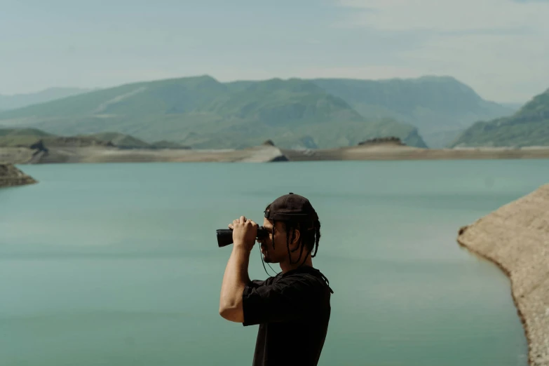 a man taking a picture of a large body of water, 📷 mungojerrie and rumpleteazer, binoculars, water reservoir, ash thorp khyzyl saleem
