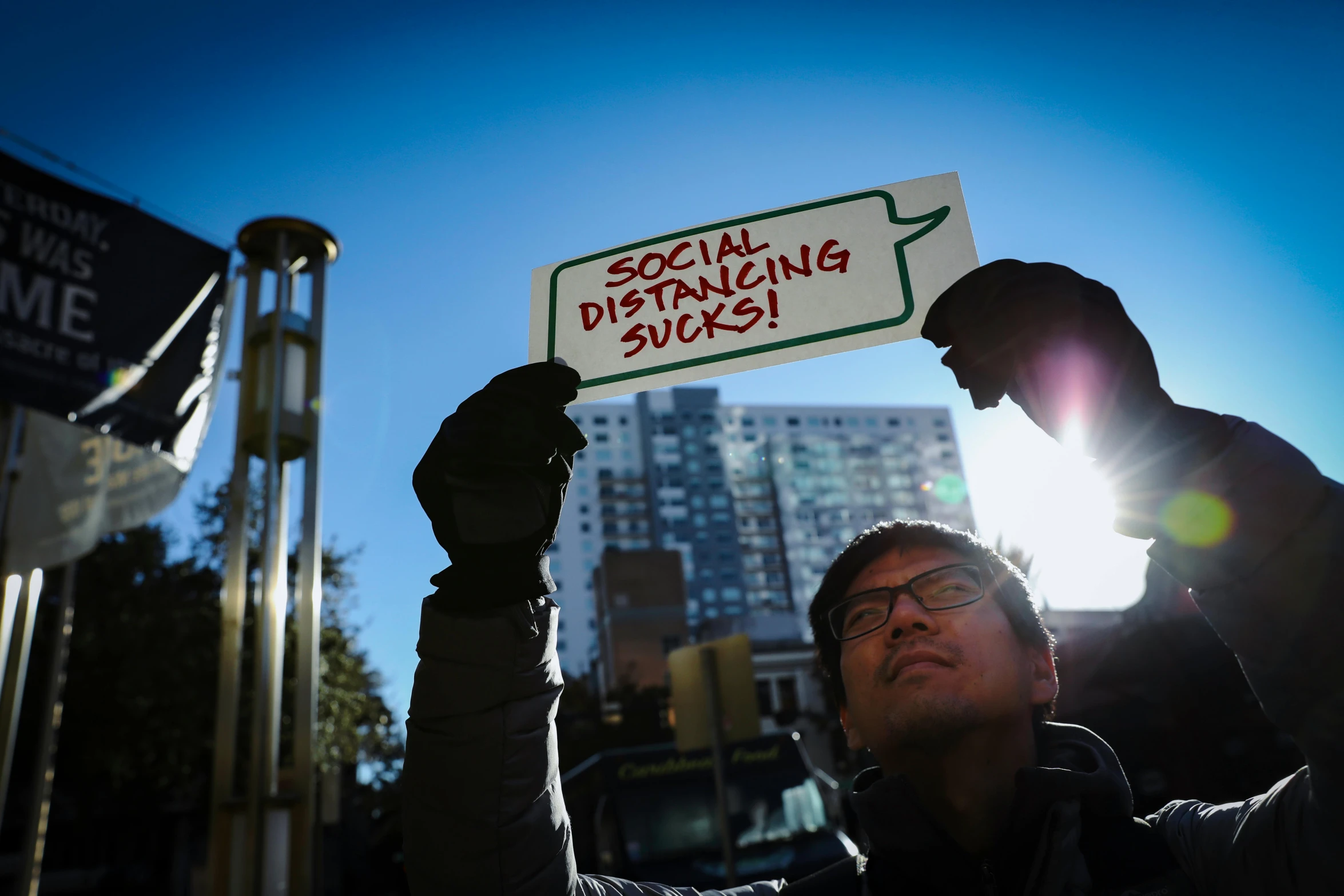 a man holding a sign that says social distancing sucks, a photo, by Julia Pishtar, square, asian descent, winter sun, photograph credit: ap