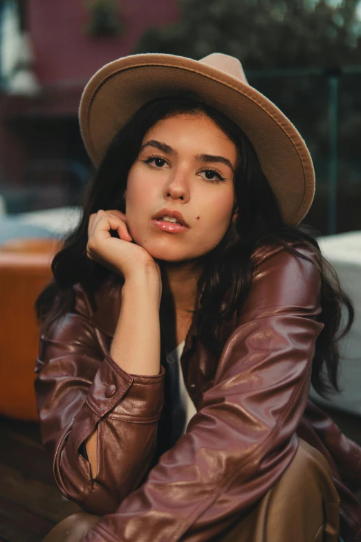 a woman sitting on a bench wearing a hat, trending on pexels, photorealism, wearing brown leather jacket, promotional image, asher duran, headshot profile picture