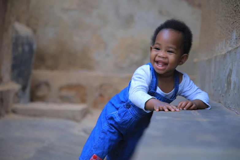 a little boy that is sitting on a ledge, pexels contest winner, happening, light skinned african young girl, blue overalls, happy and spirited expression, crawling on the ground