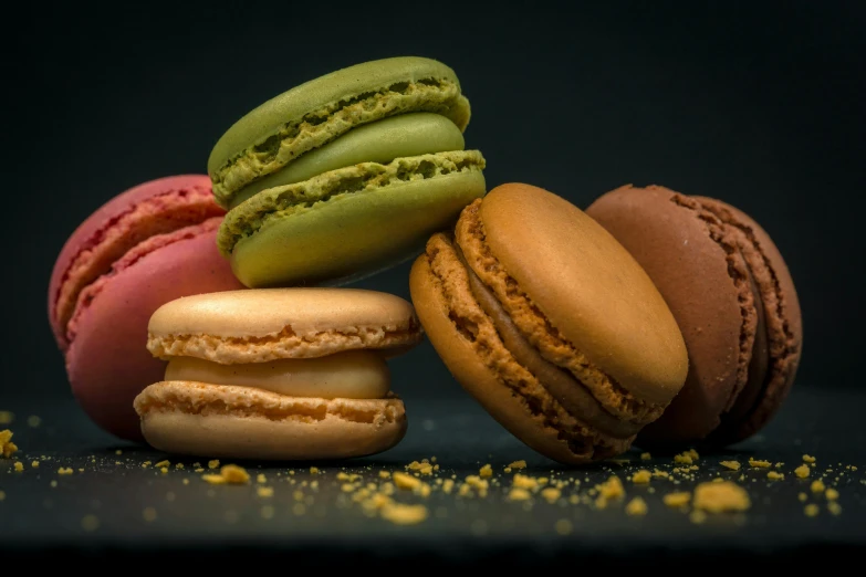 a pile of macarons sitting on top of a table, in front of a black background, 3 colours, thumbnail, snacks