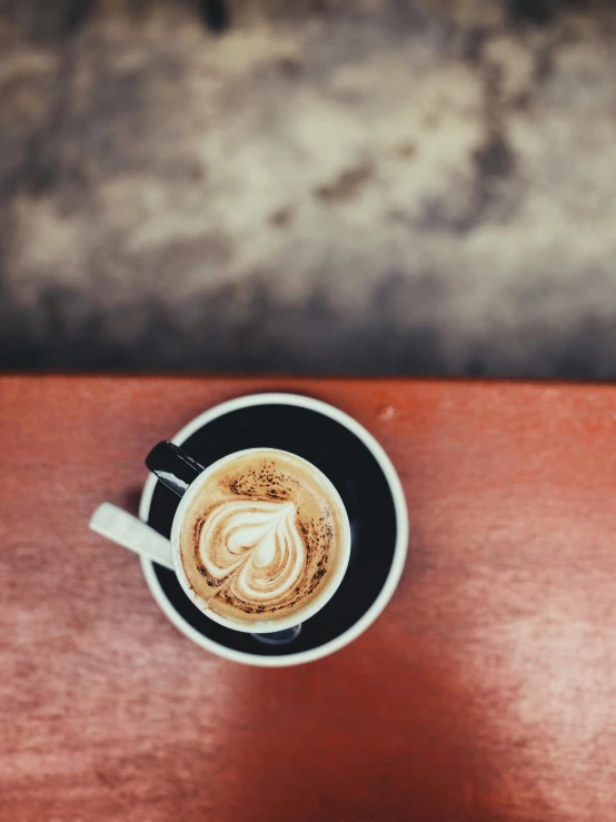 a cup of coffee sitting on top of a wooden table, by Niko Henrichon, trending on unsplash, happening, thumbnail, background image, multiple stories, latte art