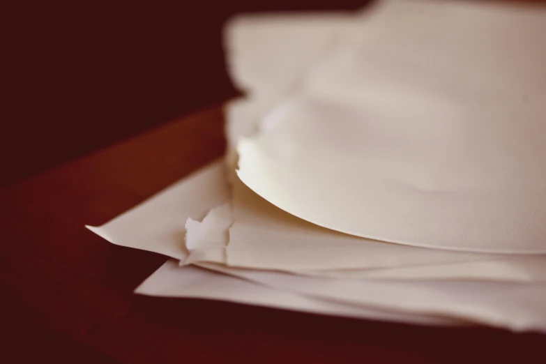 a stack of paper sitting on top of a wooden table, flowing silk sheets, cracked, writing a letter, cream paper