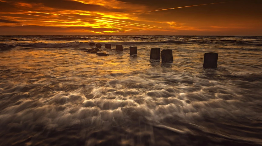 a sunset over the ocean with wooden posts in the water, by Daniel Seghers, unsplash contest winner, towering waves, thumbnail, high quality photo, fallen columns