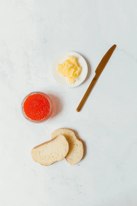 a table topped with slices of bread next to a knife, red caviar instead of sand, jen atkin, white background and fill, butter