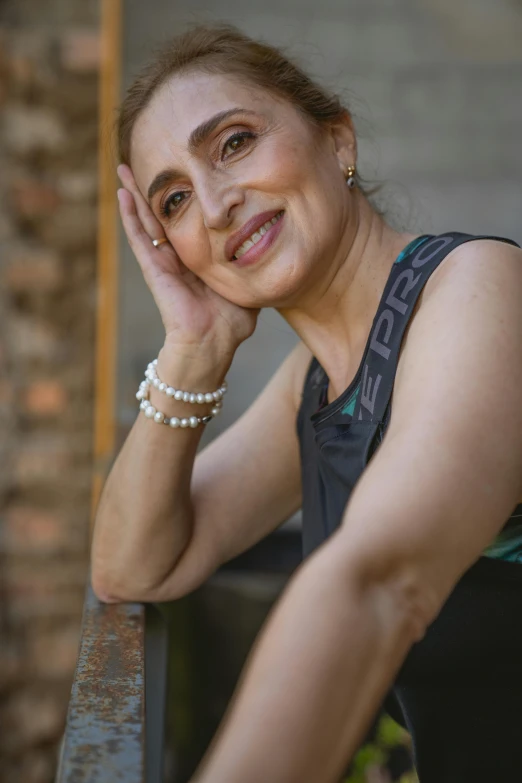 a woman leaning on a railing with her hand on her head, inspired by Lubna Agha, wearing fitness gear, she is about 6 0 years old, headshot profile picture, high view