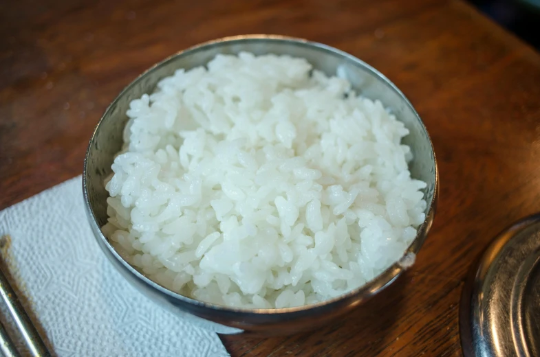 a bowl of rice sitting on top of a wooden table, pearl silverplate, crisp face, medium, ready to eat