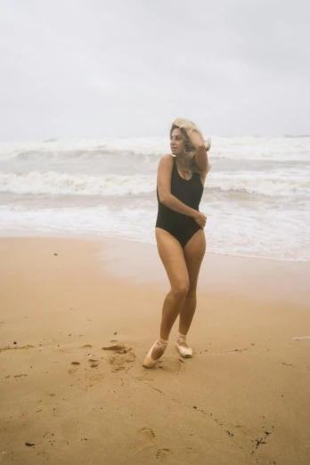 a woman running on a beach next to the ocean, an album cover, unsplash, renaissance, black swimsuit, casual pose, big overcast, in retro swimsuit