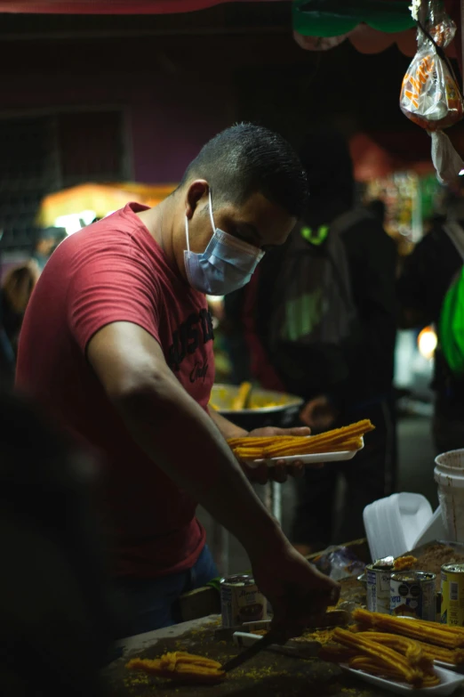 a man standing in front of a table filled with food, the masks come off at night, serving fries, downtown mexico, surgical mask covering mouth