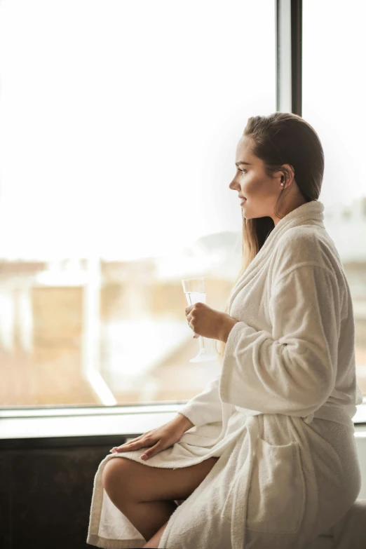 a woman in a bathrobe sitting on a window sill, trending on unsplash, drinking champagne, spa, multiple stories, pondering