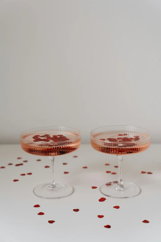 a couple of wine glasses sitting on top of a table, rose gold heart, decadence, poppy, from side