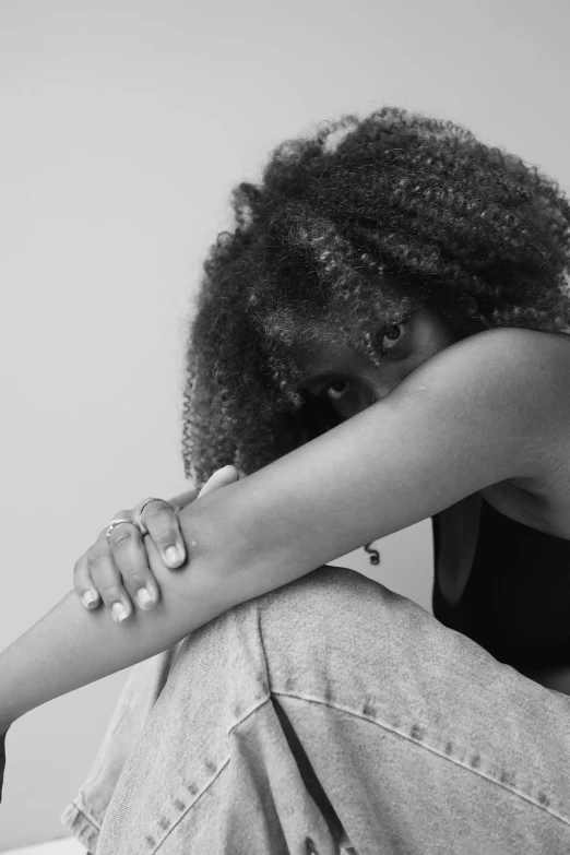 a black and white photo of a woman sitting on a bed, by Lily Delissa Joseph, sitting with wrists together, black teenage girl, curls, heartbroken