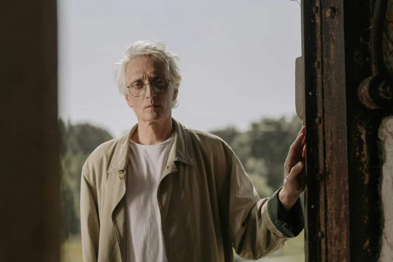 a man that is standing in front of a door, an album cover, inspired by roger deakins, pexels, photorealism, wearing silver hair, man with glasses, crewdson, matthew mcconaughey