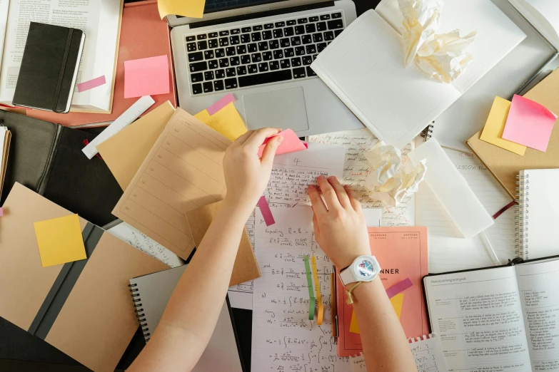 a person sitting at a desk in front of a laptop, by Julia Pishtar, trending on pexels, process art, piles of paperwork, [ overhead view of a table ]!!, school curriculum expert, with a bunch of stuff