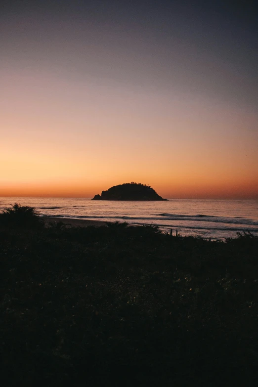 a man standing on top of a beach next to the ocean, unsplash, romanticism, evening at dusk, an island floating in the air, chile, low quality photo