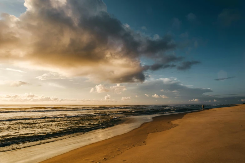 a person riding a surfboard on top of a sandy beach, by Sebastian Spreng, pexels contest winner, sunset with cloudy skies, sri lankan landscape, footprints in the sand, gold coast australia