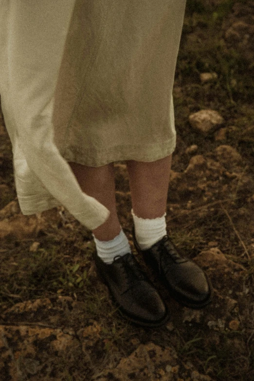 a man standing on top of a grass covered field, an album cover, inspired by Andrew Wyeth, unsplash, wearing skirt and high socks, detail shot, ignant, linen