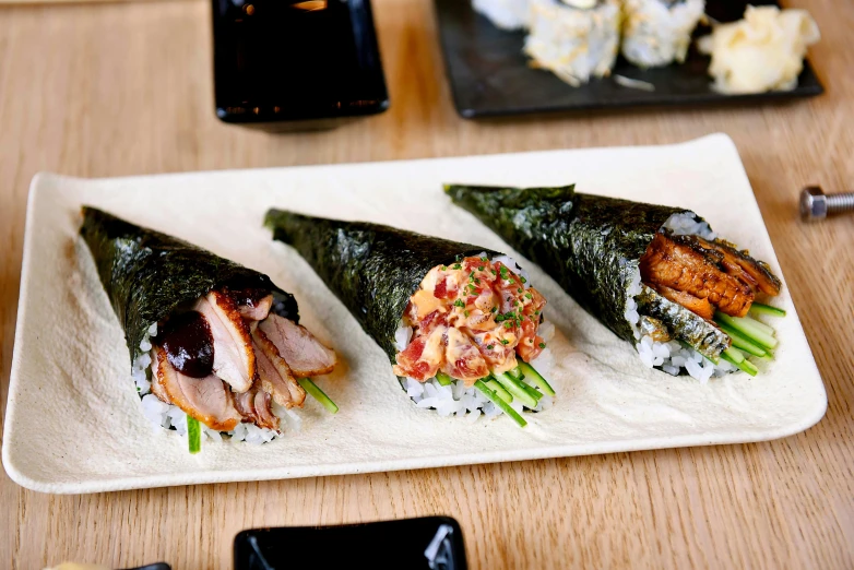 a white plate topped with sushi on top of a wooden table, cone, 3 heads, ivy's, lined up horizontally