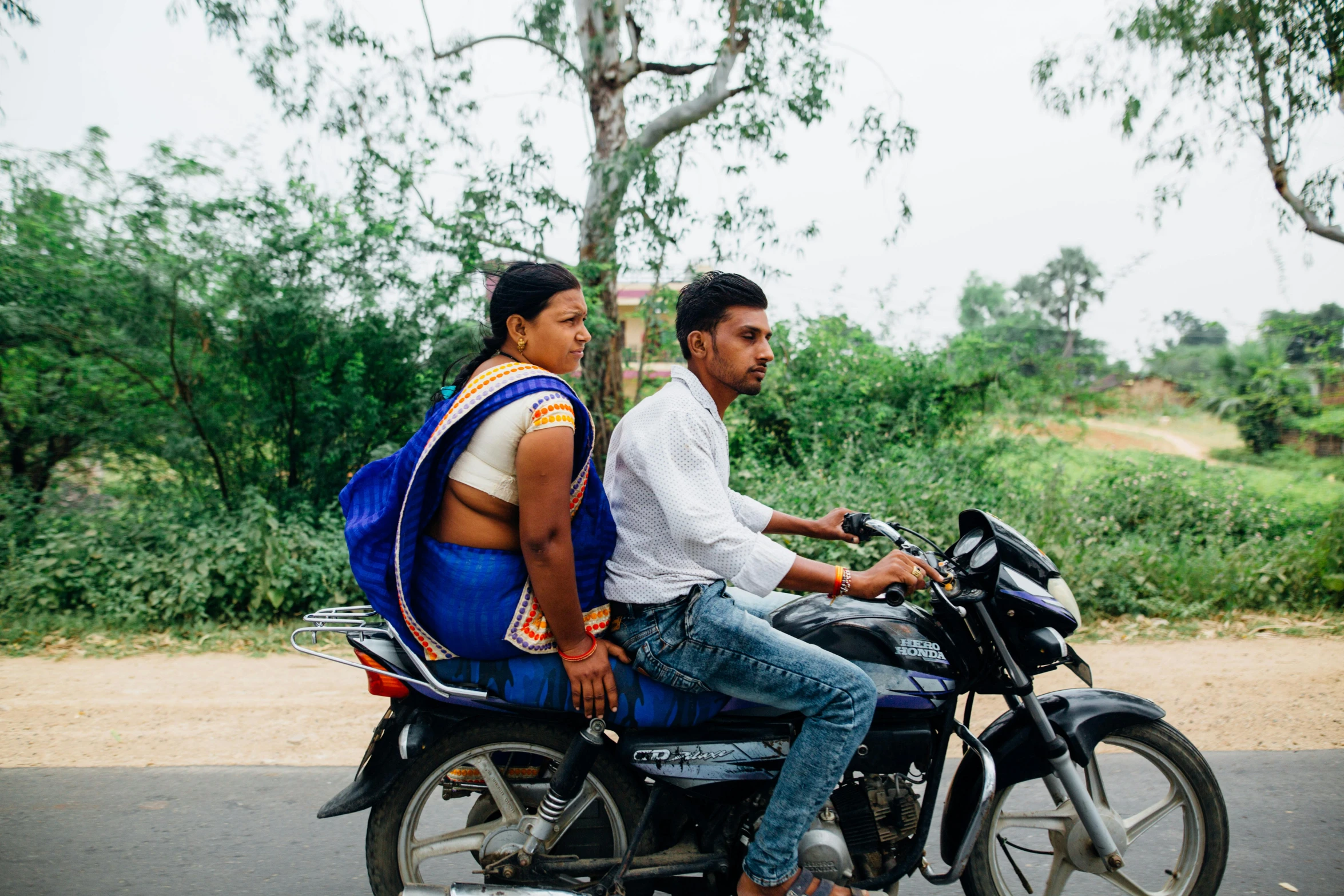 a man and a woman riding on the back of a motorcycle, by Carey Morris, samikshavad, profile image, colourful clothing, breeding, roadside