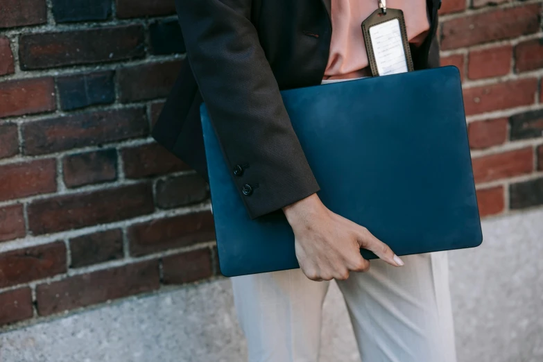 a woman standing in front of a brick wall holding a laptop, by Carey Morris, trending on unsplash, wearing dark blue suit, leather pouch, rectangle, holding a clipboard