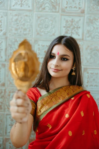 a woman in a red sari holding a mirror, pexels contest winner, renaissance, 18 years old, wearing traditional garb, avatar image, holding gold