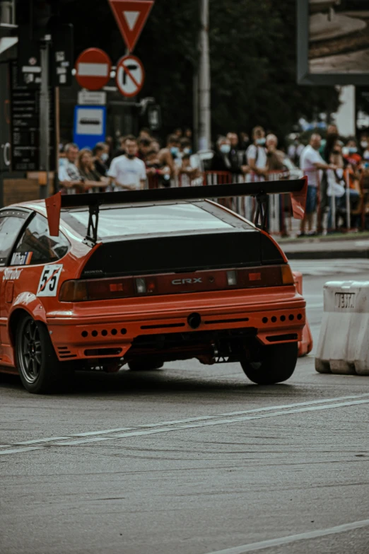 a red car driving down a street next to a crowd of people, pexels contest winner, hypermodernism, toyota jzx 1 0 0 drift, orange racing stripes, honda nsx, vintage photo